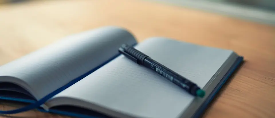 An open lined notebook with a pen across it on a timber desk
