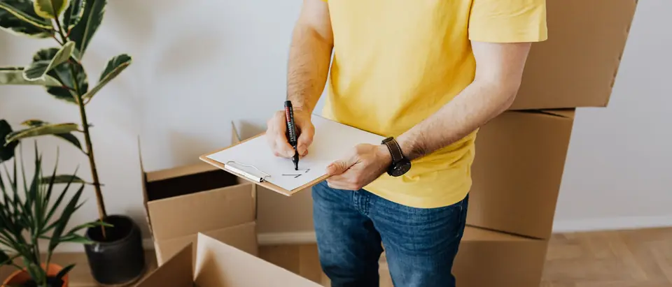 A person in a yellow T-shirt ticking a list on a clipboard beside open and stacked cartons