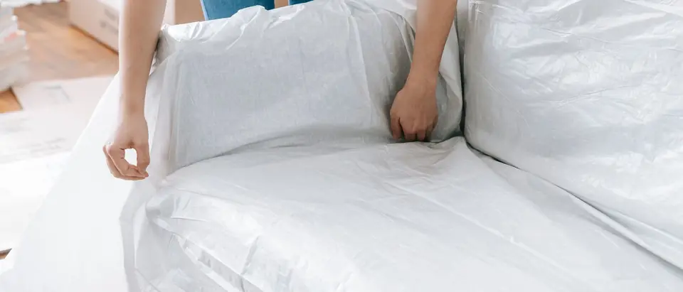 Hands smoothing a white protective cover over a sofa