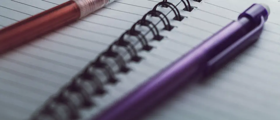 Two pens resting on an open spiral notebook